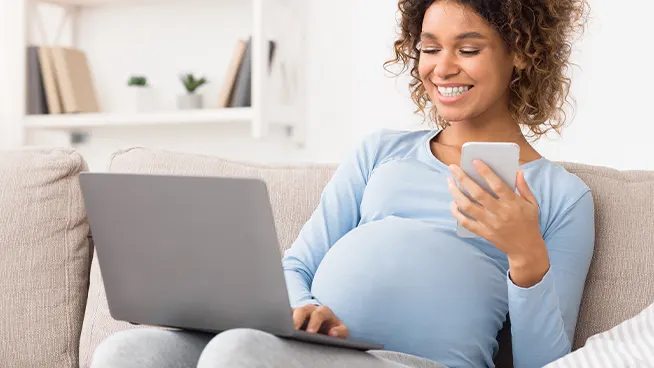 Pregnant mom holding phone and looking at laptop