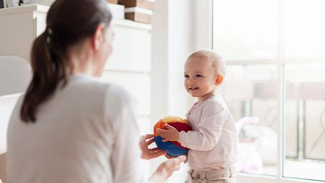 Toddler holding beach ball toy and looking at mom