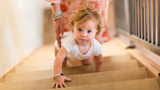 Toddler boy crawling up the stairs as his mom follows behind him