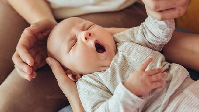 Mom holding yawning baby in her lap