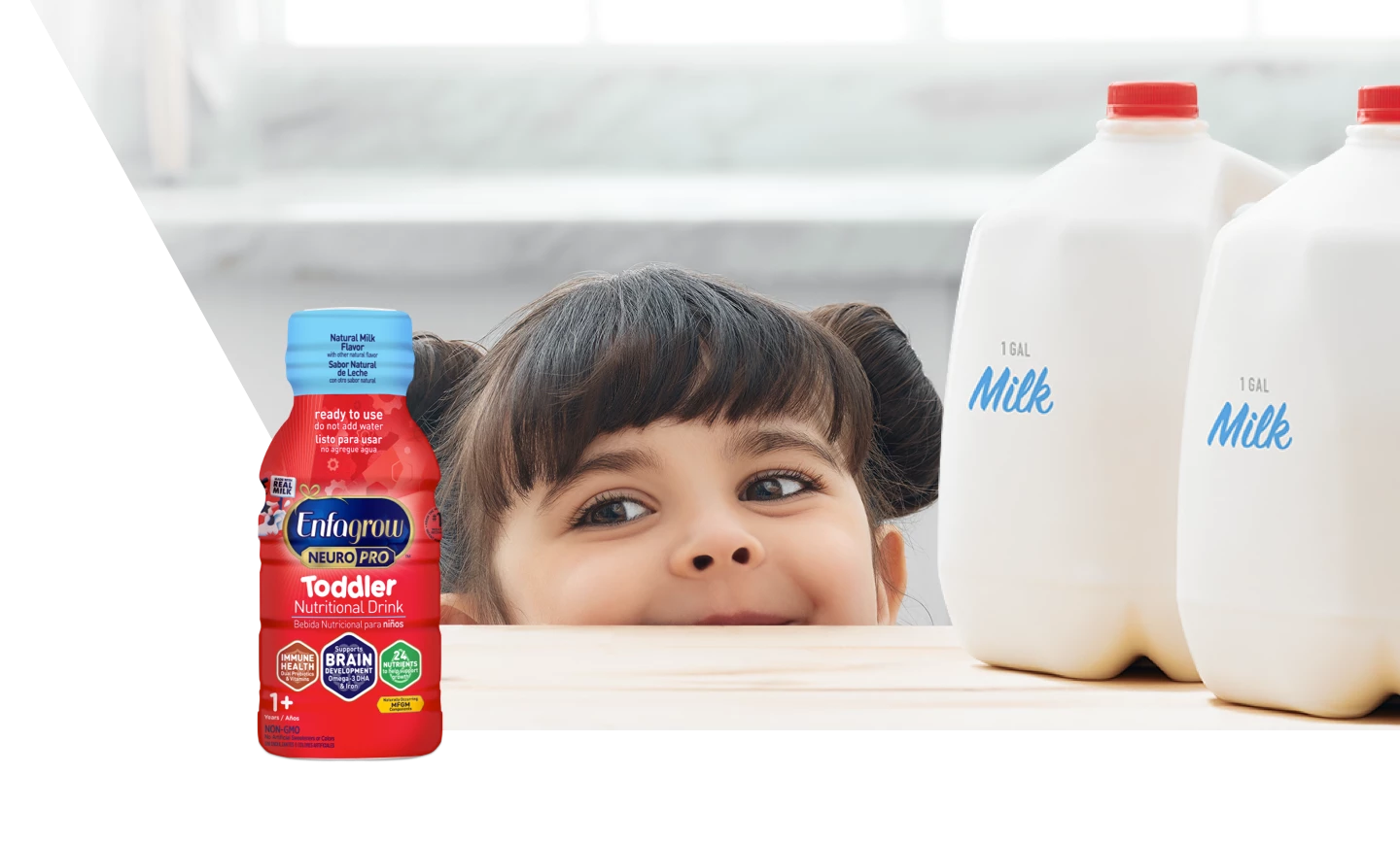Toddler girl peaking over the counter looking at Enfagrow® PREMIUM Toddler Nutritional Drink