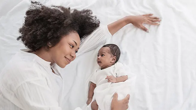 Mom laying on a bed looking lovingly at newborn infant