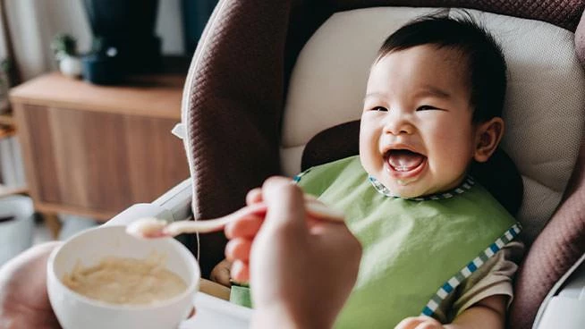 Smiling baby in a high chair being spoon-fed