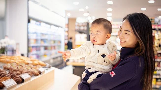 Mamá sosteniendo a un niño pequeño que señala la comida en el supermercado