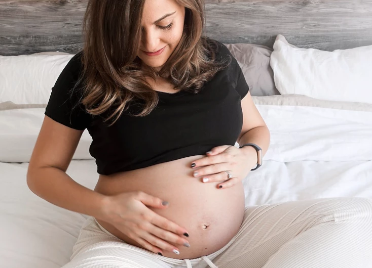 Smiling pregnant woman sitting on her bed holding her belly