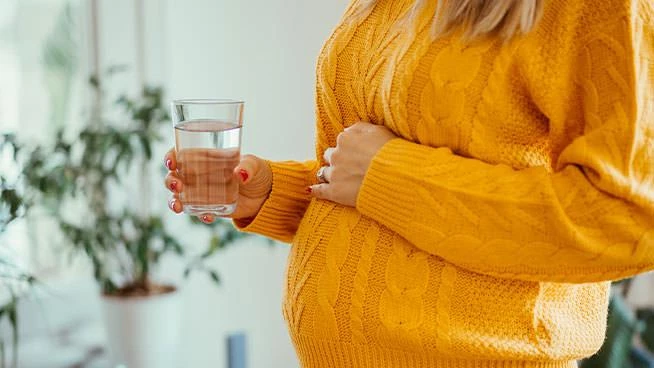 Pregnant mom holding her belly and holding a glass of water