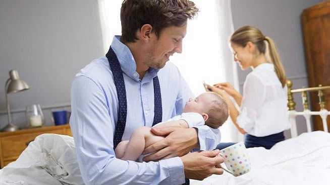 Dad holding baby while mom gets ready for work