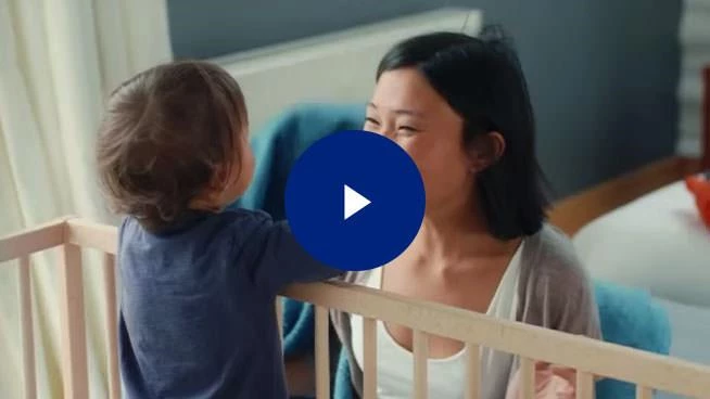 Mom smiling at toddler in a crib image with play button overlay