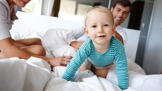 Toddler crawling on the bed with dad and mom