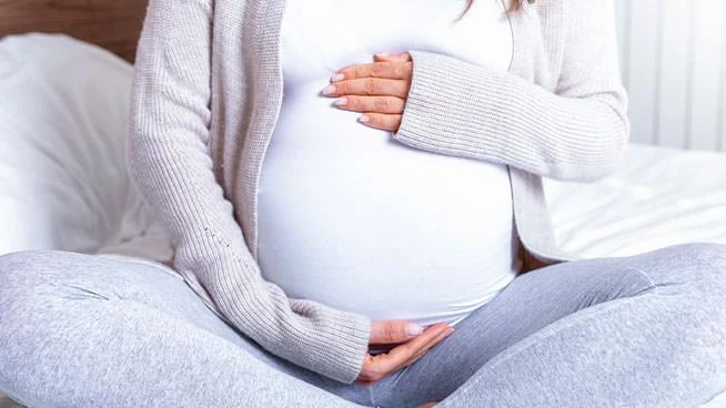 Mamá embarazada sentada con las piernas cruzadas sosteniendo su vientre