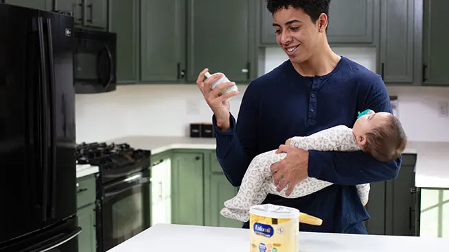 Dad checking bottle while cradling baby