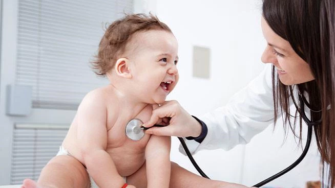 Pediatra escuchando el pecho del bebé feliz