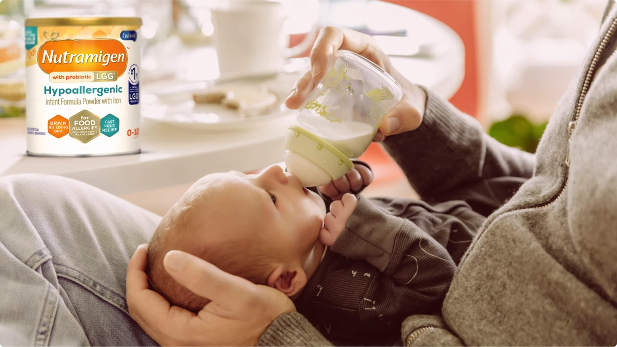 Dad feeding baby a bottle with Nutramigen® with Probiotic LGG® Hypoallergenic Infant Formula on the table