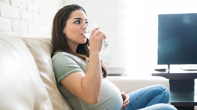Pregnant woman sitting on couch drinking a glass of water