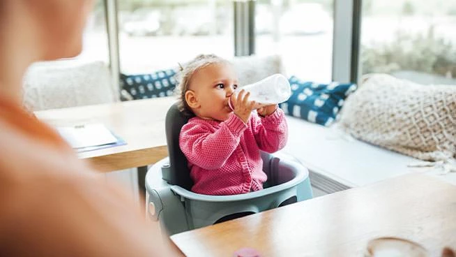 Toddler drinking formula while sitting next to parents at the dinner table