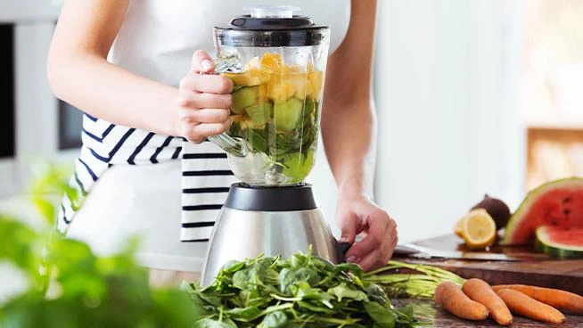 Mujer poniendo verduras en una licuadora
