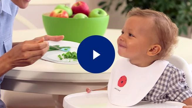 Parent spoon feeding toddler with play button overlay