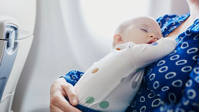 Baby sleeping against mom while they travel on a plane