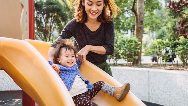 Mom helping toddler go down a slide