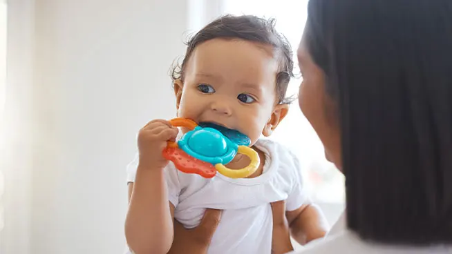 Madre sosteniendo a un bebé al que le están saliendo los dientes en un juguete colorido