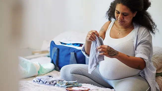 Pregnant woman packing baby clothes on bed