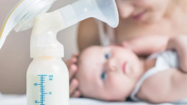 Extractor manual lleno de leche materna sentado frente a la mamá y el bebé