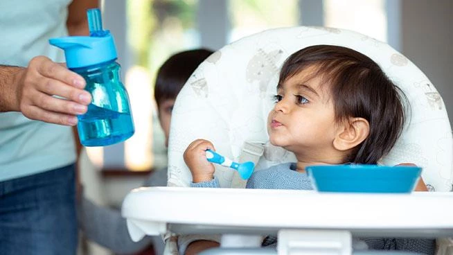 Toddler in a high chair receiving sippy cup from parent