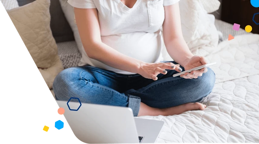 Pregnant woman scrolling on her phone with her laptop open in front of her