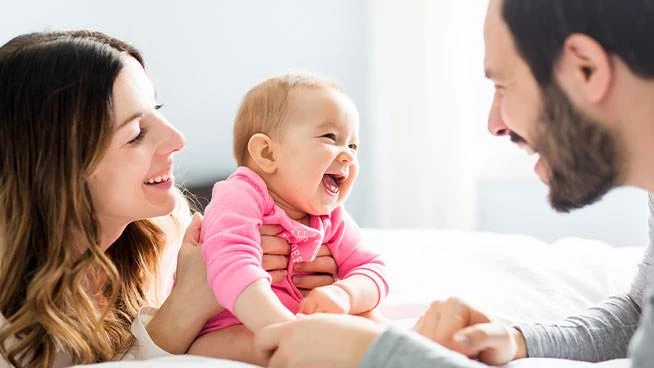 Dad and mom smiling with baby on the bed