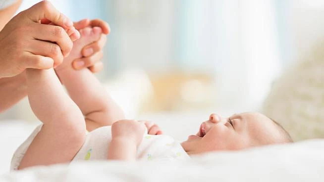 Bebé feliz acostado boca arriba mientras mamá sostiene sus pies