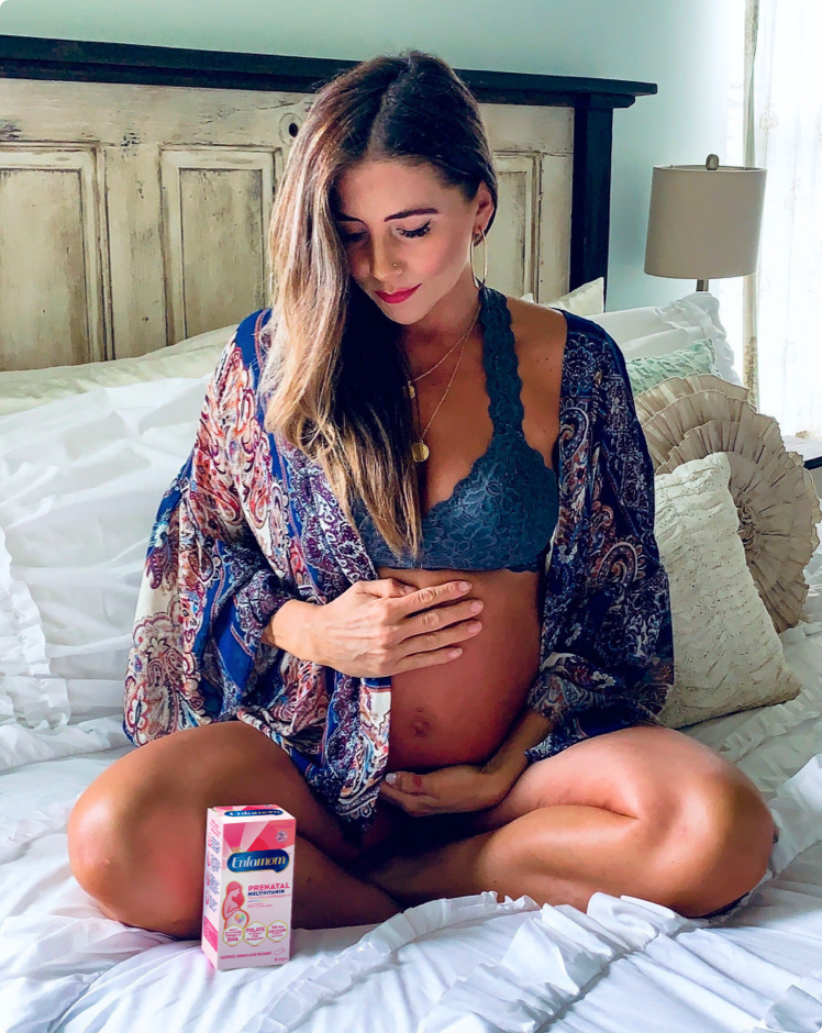 Mujer embarazada sentada en la cama con vitaminas prenatales Enfamom™