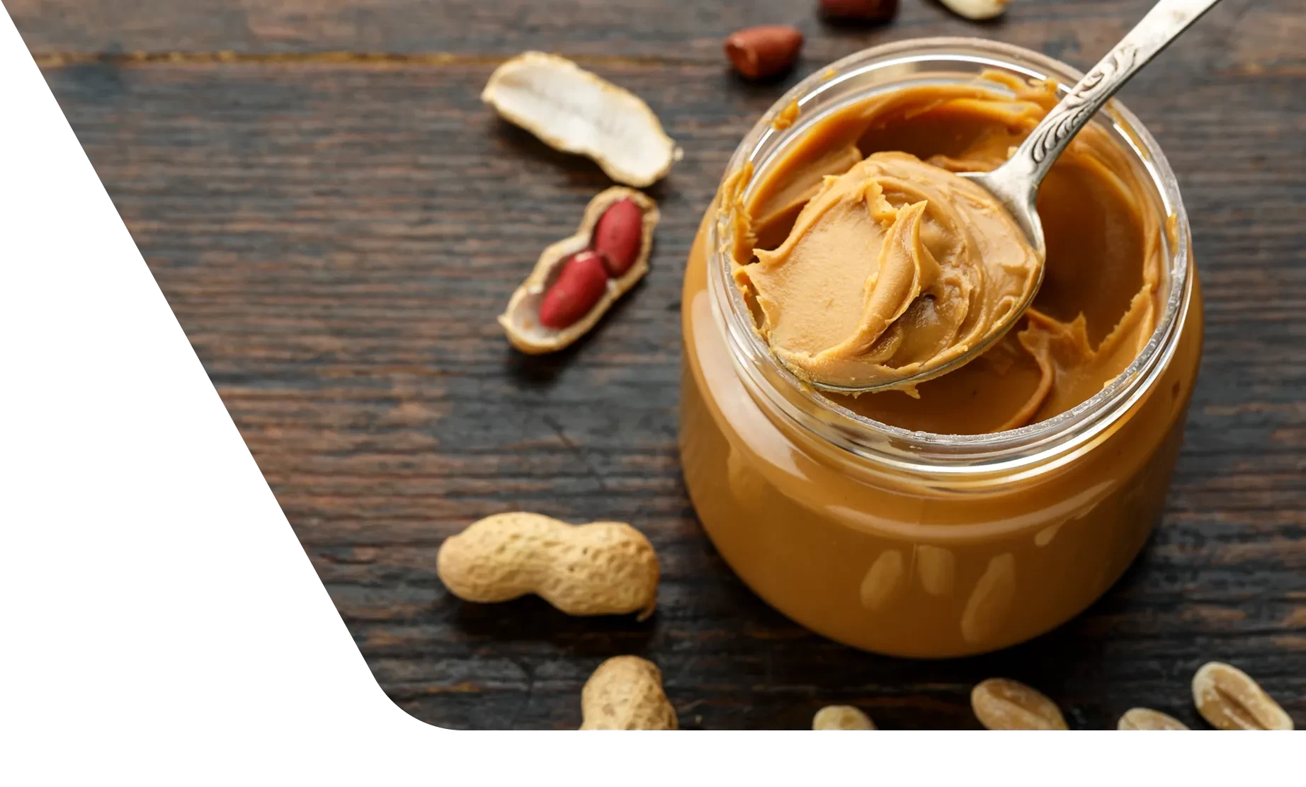 A jar of peanut butter with a spoon-full of peanut butter sitting on top of the jar