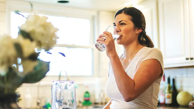 Mujer parada en la cocina, bebiendo un vaso de agua