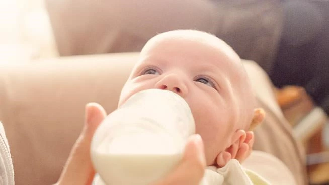 Close up of an infant looking up while drinking out of baby bottle
