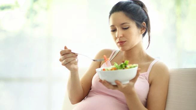 Pregnant mom sitting on the couch eating a salad