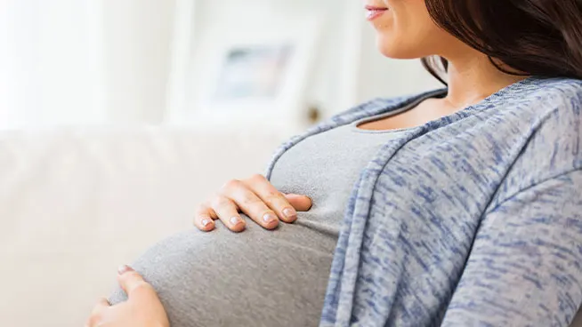 Mujer embarazada sentada, con ambas manos apoyadas en el vientre