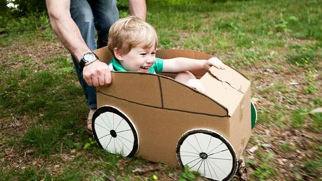 Niño pequeño jugando a fingir en un auto de cartón con papá