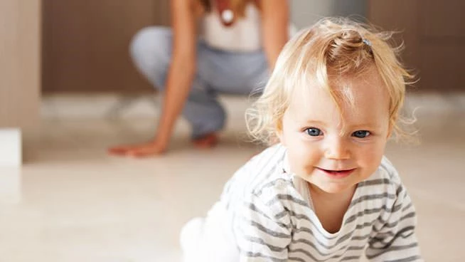 Bebé sonriente gateando mientras mamá mira detrás