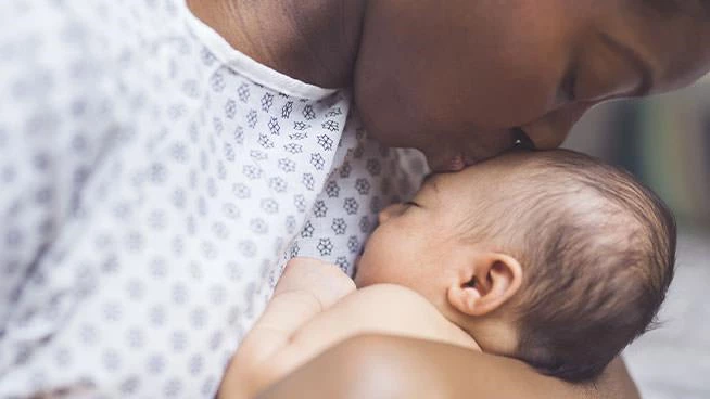 Madre en bata de hospital besando la cabeza de su bebé recién nacido