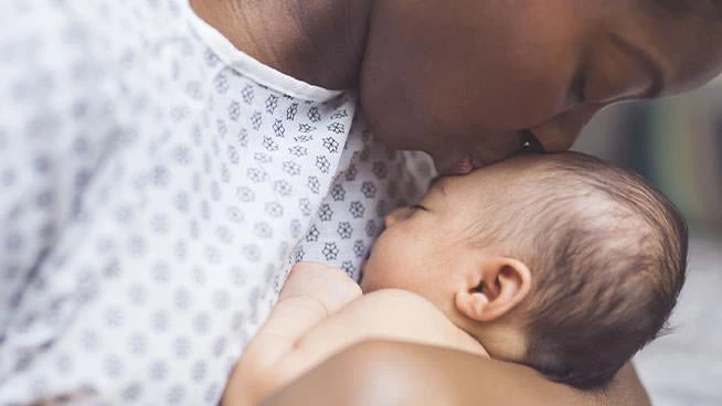Mom in hospital gown kissing newborn baby