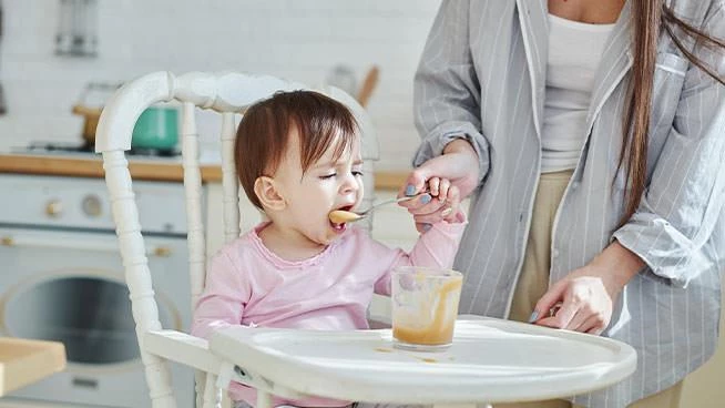 Toddler in a high chair eating with a spoon