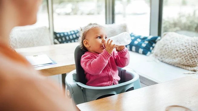Baby sitting in a highchair drinking a bottle