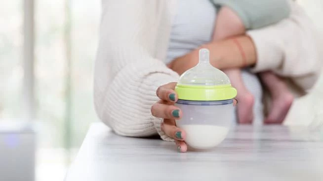 Mom reaching for bottle on the counter with baby in her arms