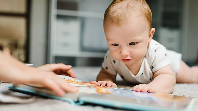 Baby looking at a colorful book with parent nearby