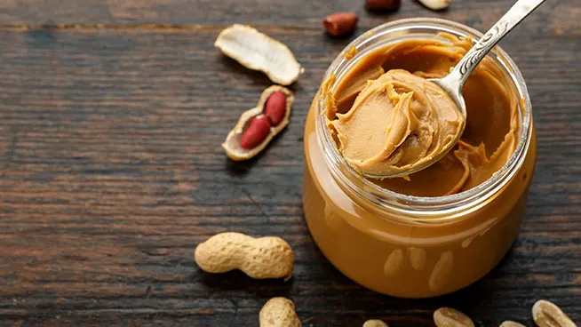 A jar of peanut butter with a spoon-full of peanut butter sitting on top of the jar